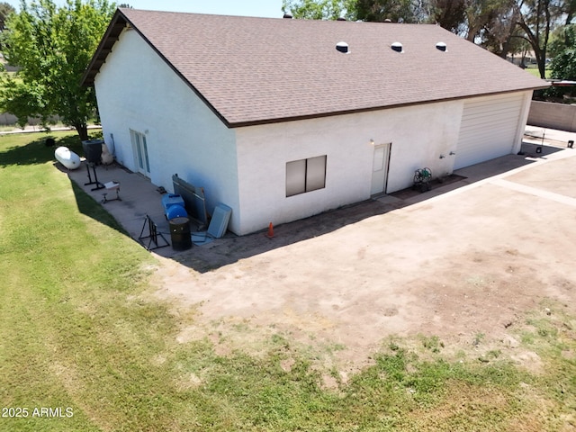 back of house featuring stucco siding, roof with shingles, a yard, and a garage