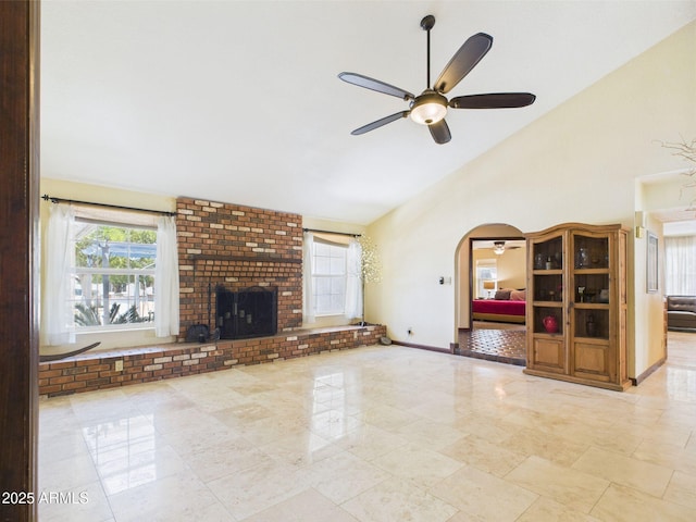 unfurnished living room with a ceiling fan, arched walkways, high vaulted ceiling, a fireplace, and baseboards