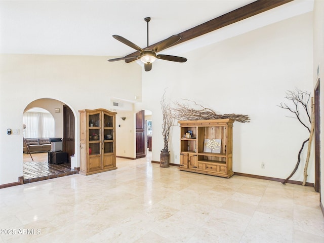 unfurnished living room featuring arched walkways, ceiling fan, high vaulted ceiling, baseboards, and beamed ceiling
