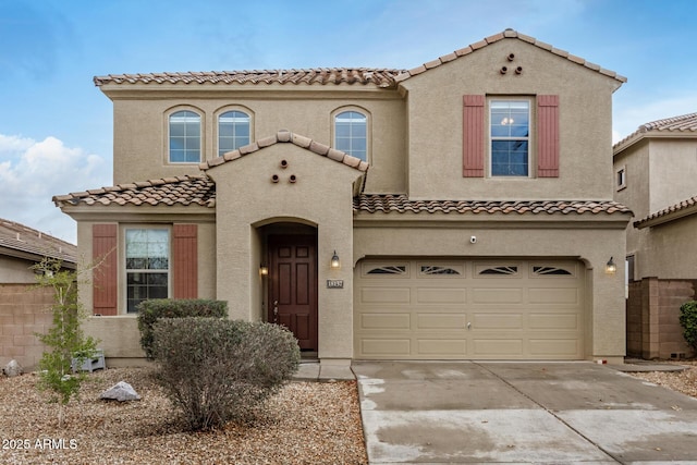 mediterranean / spanish home with a tile roof, stucco siding, an attached garage, and concrete driveway