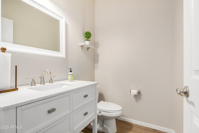 half bathroom with vanity, toilet, wood finished floors, and baseboards