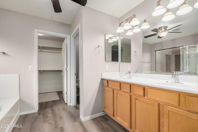 bathroom with a garden tub, double vanity, wood finished floors, a ceiling fan, and a sink