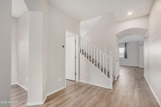 staircase featuring arched walkways, baseboards, and wood finished floors