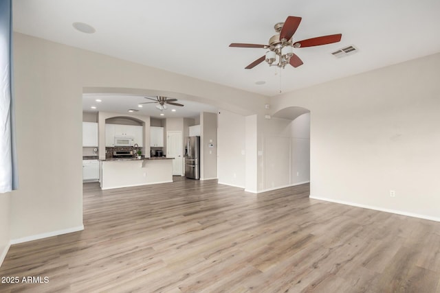 unfurnished living room with a ceiling fan, light wood-style floors, visible vents, and arched walkways