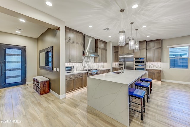 kitchen with a kitchen breakfast bar, tasteful backsplash, wall chimney exhaust hood, pendant lighting, and an island with sink