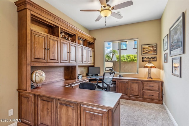 office featuring light carpet, ceiling fan, built in desk, and baseboards