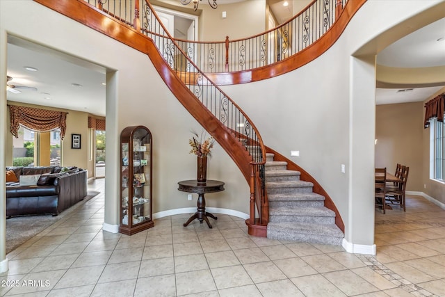 stairway with arched walkways, tile patterned floors, a towering ceiling, and baseboards