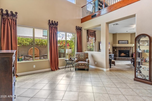 sitting room with tile patterned flooring, visible vents, a towering ceiling, baseboards, and a tiled fireplace