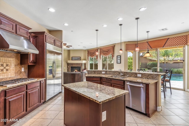 kitchen with under cabinet range hood, stainless steel appliances, a sink, dark brown cabinets, and an island with sink