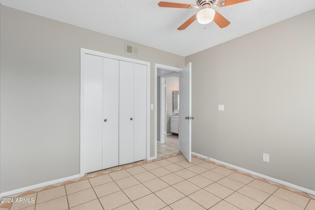 unfurnished bedroom with light tile patterned flooring, a textured ceiling, a closet, and ceiling fan