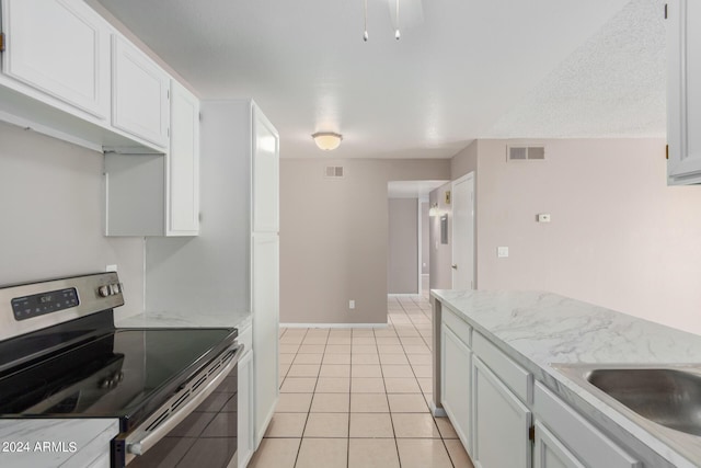 kitchen with white cabinets, a textured ceiling, light tile patterned floors, and electric stove