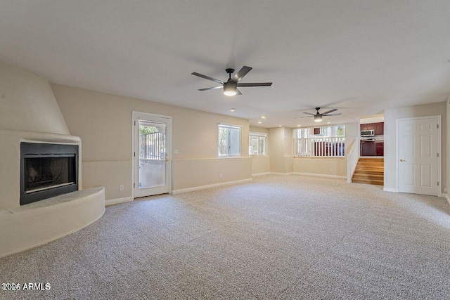 unfurnished living room featuring a wealth of natural light, light carpet, a fireplace, and baseboards