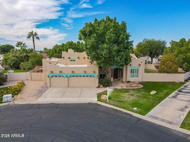 pueblo-style home featuring a garage, fence, driveway, stucco siding, and a front lawn