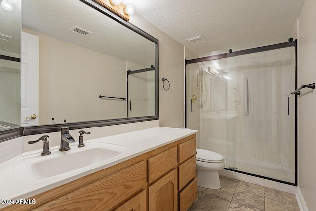 bathroom featuring visible vents, toilet, vanity, a shower stall, and a textured ceiling