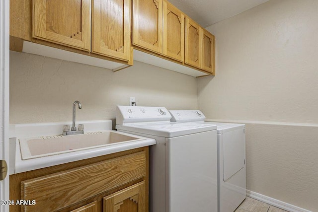 laundry area with a textured wall, washing machine and dryer, a sink, baseboards, and cabinet space