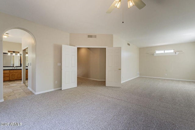 unfurnished bedroom featuring arched walkways, connected bathroom, light colored carpet, visible vents, and baseboards