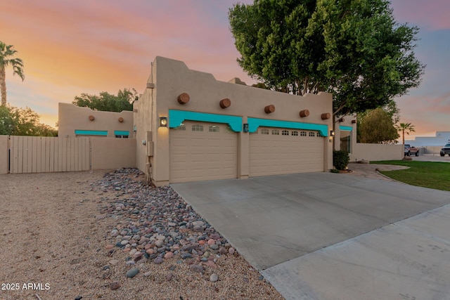 adobe home with a garage, fence, driveway, a gate, and stucco siding