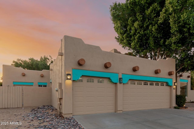 garage at dusk with concrete driveway and fence