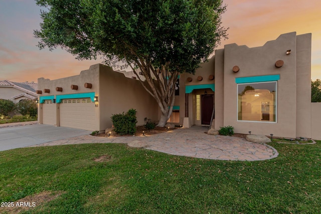 pueblo-style home with a garage, concrete driveway, a yard, and stucco siding