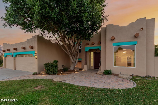 pueblo revival-style home featuring driveway, a front lawn, an attached garage, and stucco siding