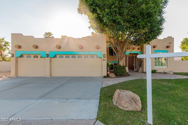 pueblo-style house featuring an attached garage, a front lawn, concrete driveway, and stucco siding