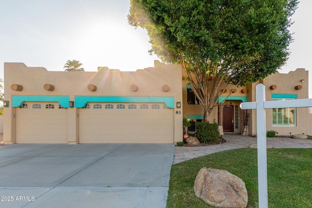 pueblo-style home featuring driveway, an attached garage, and stucco siding