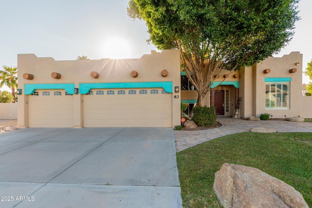 pueblo revival-style home with a garage, concrete driveway, and stucco siding