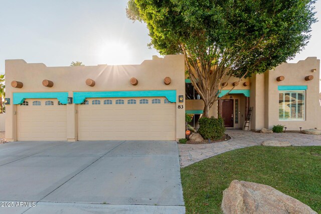 pueblo-style home with a garage, concrete driveway, and stucco siding