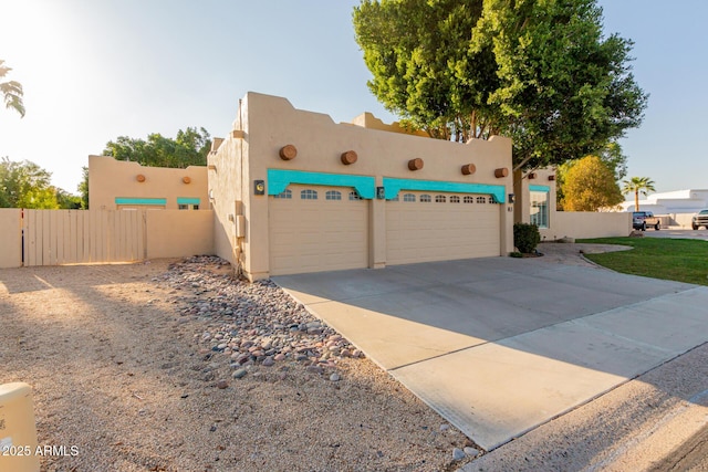 adobe home with driveway, an attached garage, fence, and stucco siding