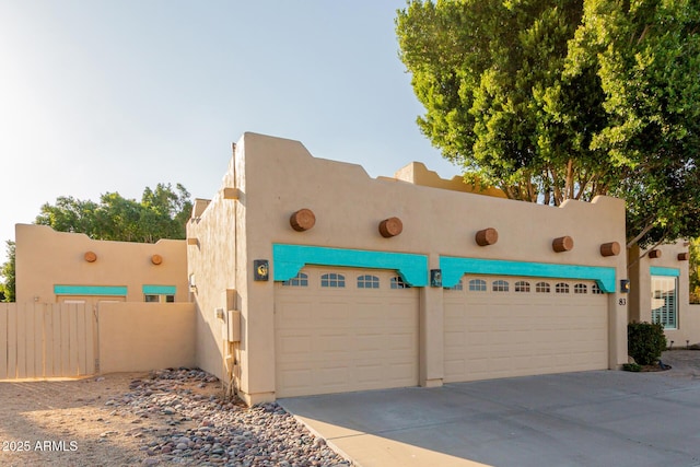 view of front of house featuring driveway, an attached garage, fence, and stucco siding