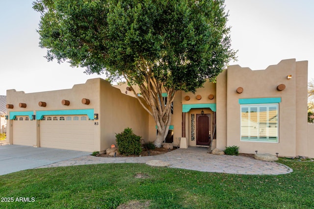 adobe home featuring concrete driveway, a front yard, and stucco siding