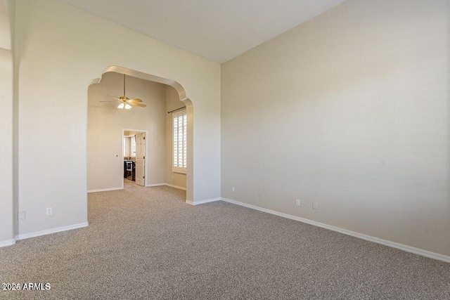 carpeted empty room with high vaulted ceiling, ceiling fan, arched walkways, and baseboards