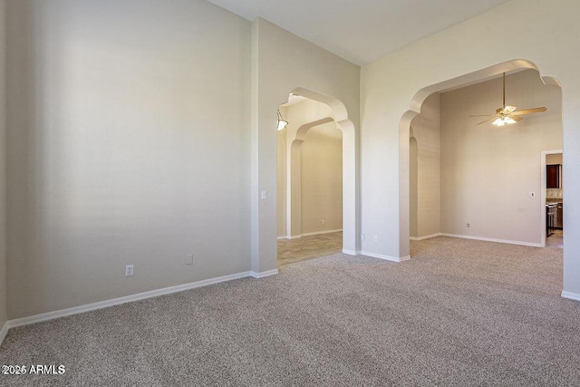 spare room with arched walkways, carpet, a ceiling fan, and baseboards