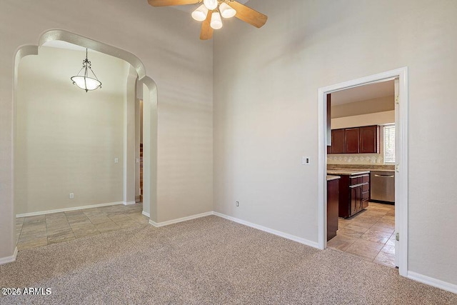 unfurnished room with a ceiling fan, arched walkways, light carpet, and baseboards