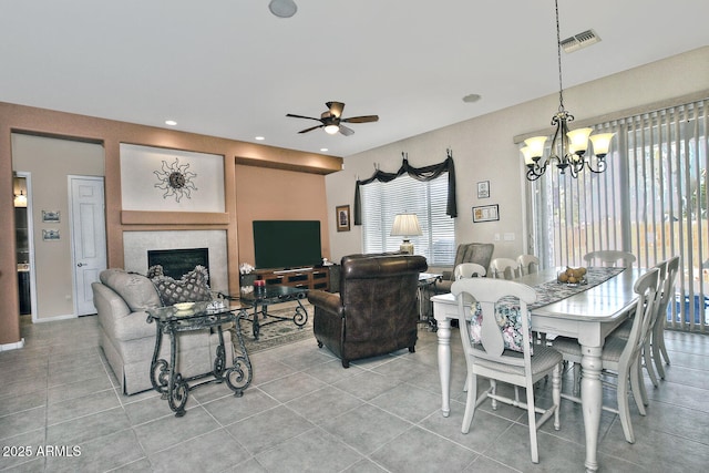 dining space featuring light tile patterned floors, ceiling fan with notable chandelier, and a tiled fireplace