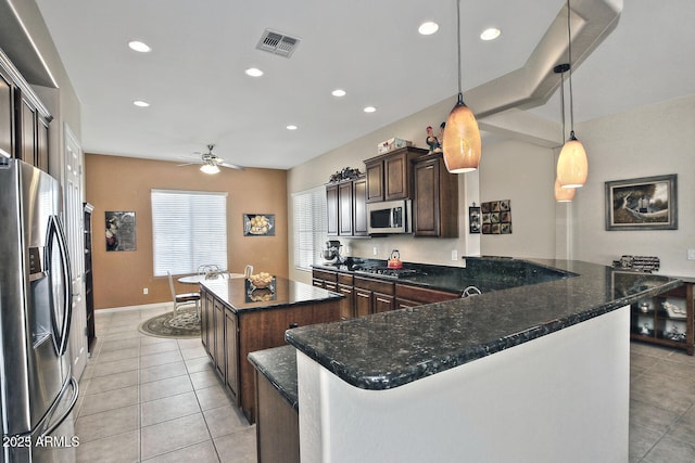 kitchen featuring dark brown cabinetry, hanging light fixtures, kitchen peninsula, dark stone countertops, and appliances with stainless steel finishes