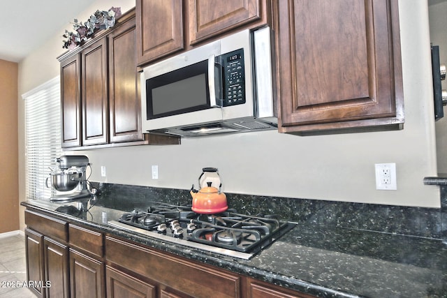 kitchen featuring gas cooktop, light tile patterned floors, dark brown cabinetry, and dark stone countertops