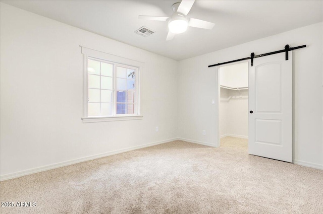 unfurnished bedroom featuring ceiling fan, a spacious closet, a barn door, light carpet, and a closet