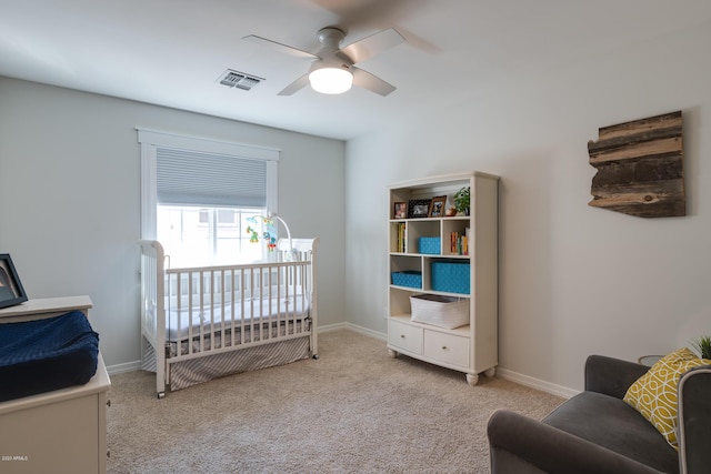 bedroom featuring a crib, light colored carpet, and ceiling fan