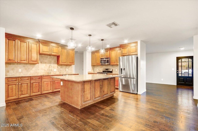 kitchen with dark wood-type flooring, hanging light fixtures, a kitchen island, and stainless steel appliances