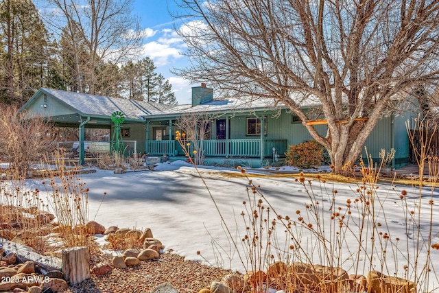 snow covered property featuring covered porch and a chimney