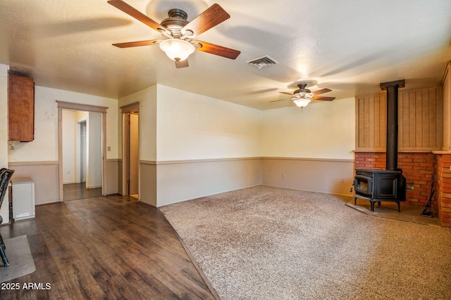 unfurnished living room featuring visible vents, ceiling fan, a wood stove, wood finished floors, and a textured ceiling