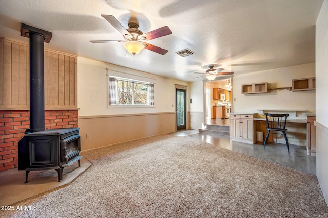 carpeted living area featuring visible vents, a textured ceiling, a wood stove, and a ceiling fan