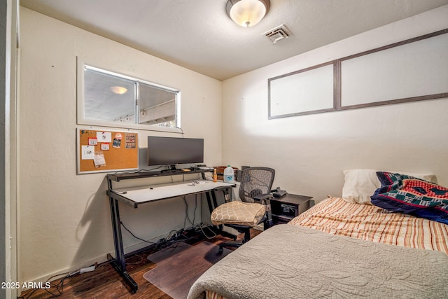 bedroom with a textured wall, visible vents, baseboards, and wood finished floors