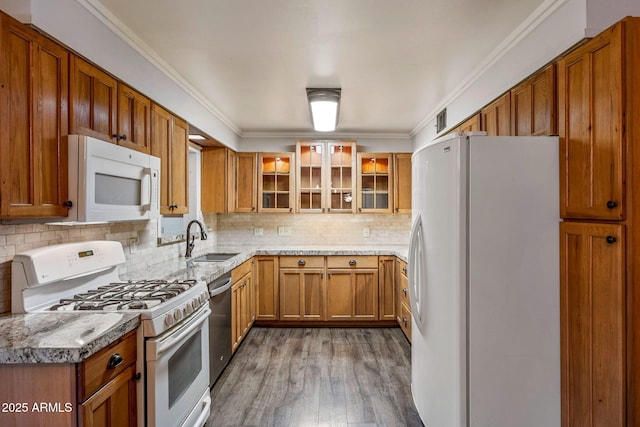 kitchen with white appliances, brown cabinetry, a sink, glass insert cabinets, and backsplash