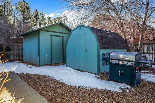 snow covered structure featuring a storage unit, an outdoor structure, and fence