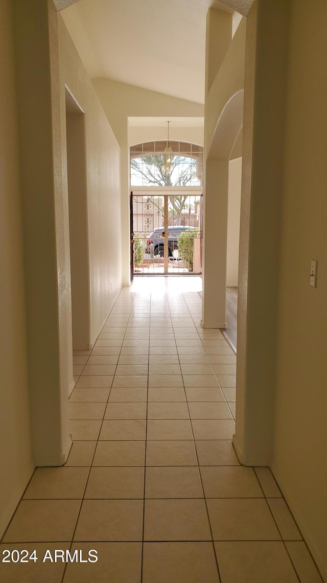 hallway featuring light tile patterned floors, lofted ceiling, and an inviting chandelier