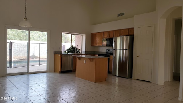 kitchen featuring a center island, a towering ceiling, decorative light fixtures, light tile patterned floors, and black appliances