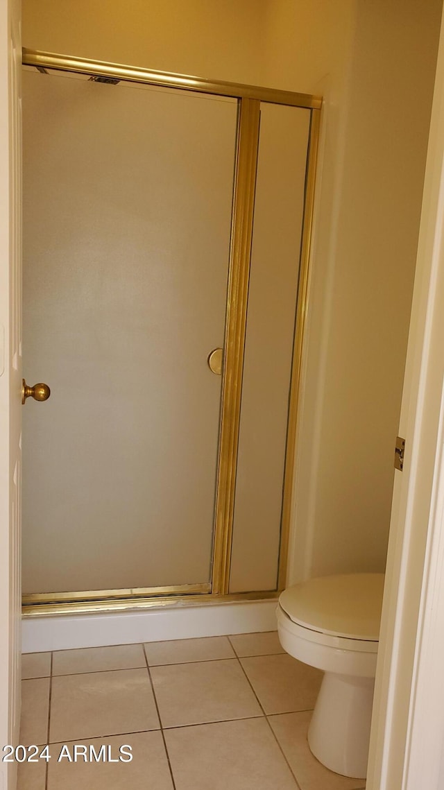 bathroom featuring tile patterned flooring, toilet, and a shower with shower door