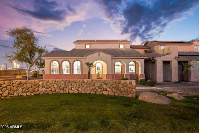 mediterranean / spanish home featuring roof mounted solar panels, stucco siding, a tile roof, and a yard